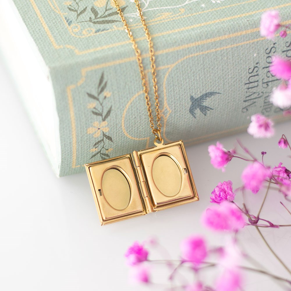 Gold book locket necklace on a decorative pillow with pink flowers