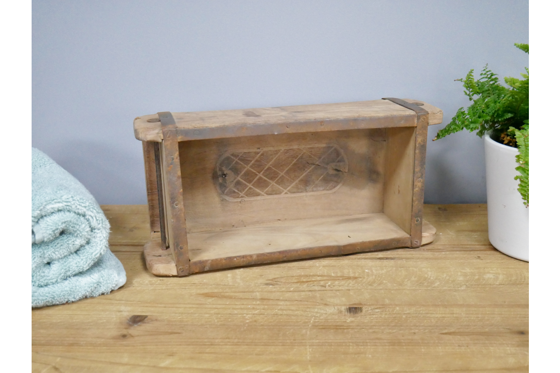 Wooden brick mould box with lattice design on a wooden surface with a light blue wall and plant in the background