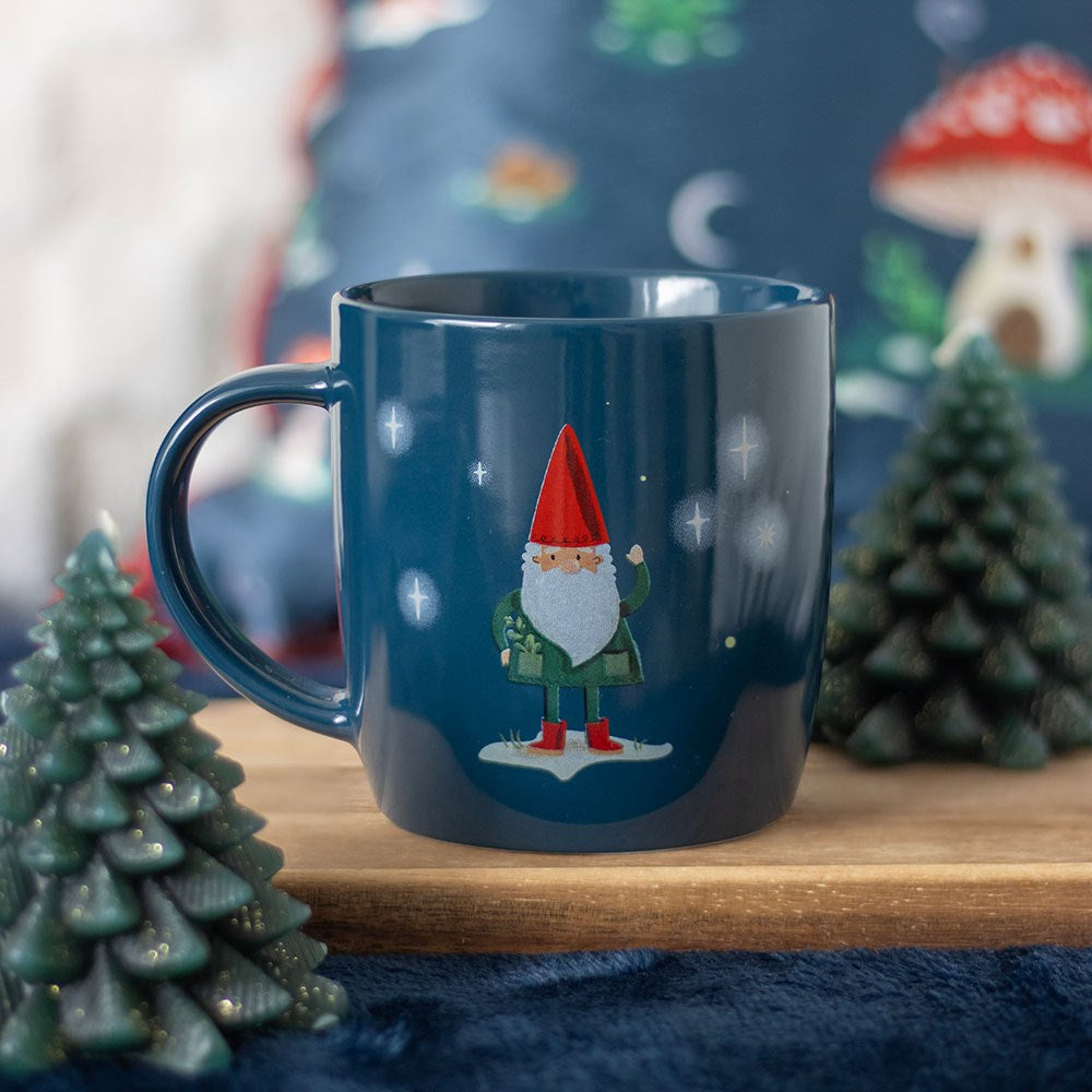 Blue mug with a gnome design on a wooden surface with Christmas decorations.