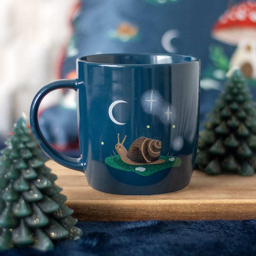 Navy blue mug with a snail and moon design on a wooden surface with decorative elements.