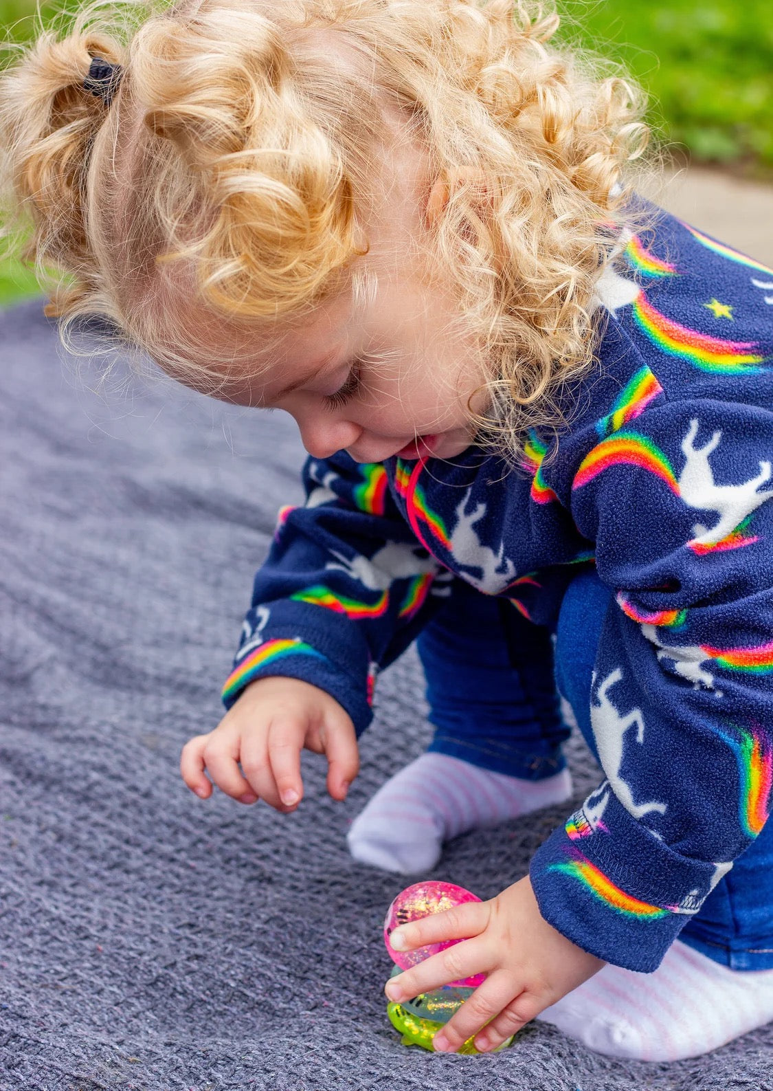 Child wearing a colourful sweater with rainbow patterns, playing outdoors with Scrunchems Sugar Squishy Kitties
