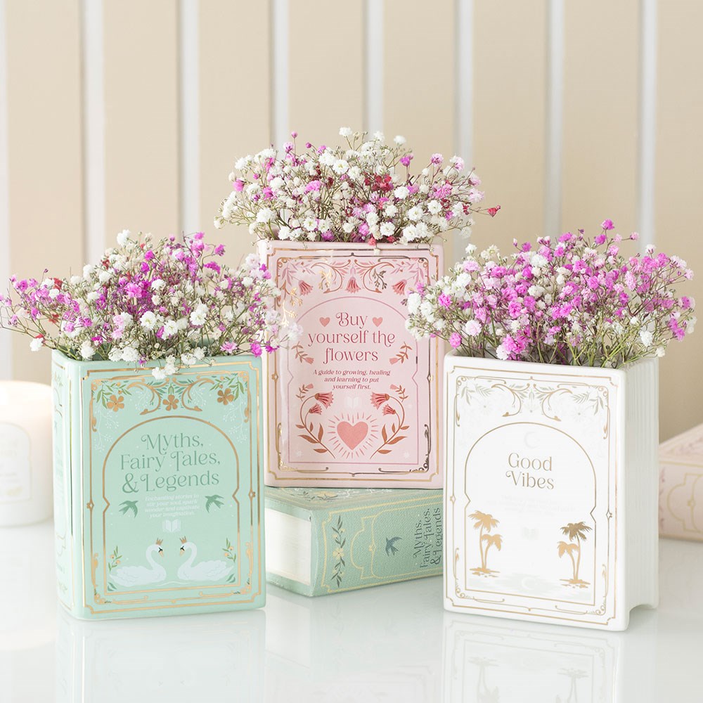 Three decorative vase planters filled with pink and white flowers, each on top of a book with text.