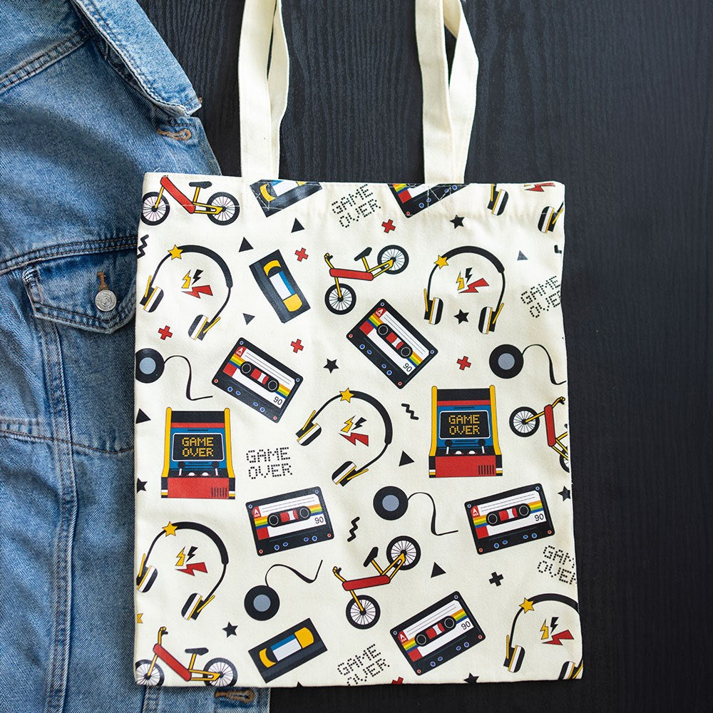 Tote bag with retro-themed design featuring cassette tapes, bikes, and 'Game Over' signs on a white background.