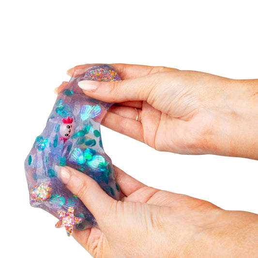 Hand holding a colorful slime toy with glittery stars and a small figure on a white background