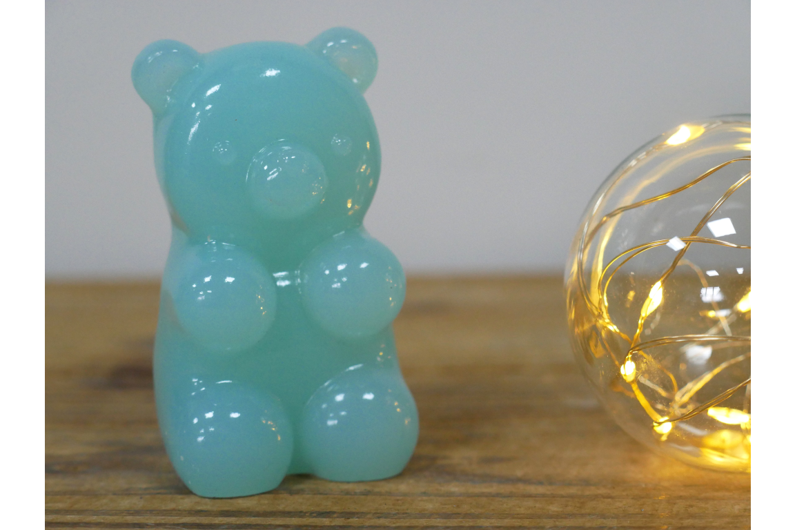 Turquoise gummy bear-shaped object on a wooden surface with a string light in the background.