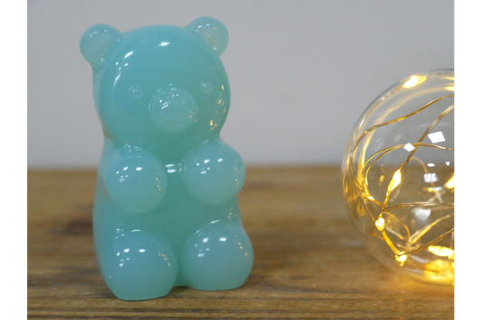Turquoise gummy bear-shaped object on a wooden surface with a string light in the background.