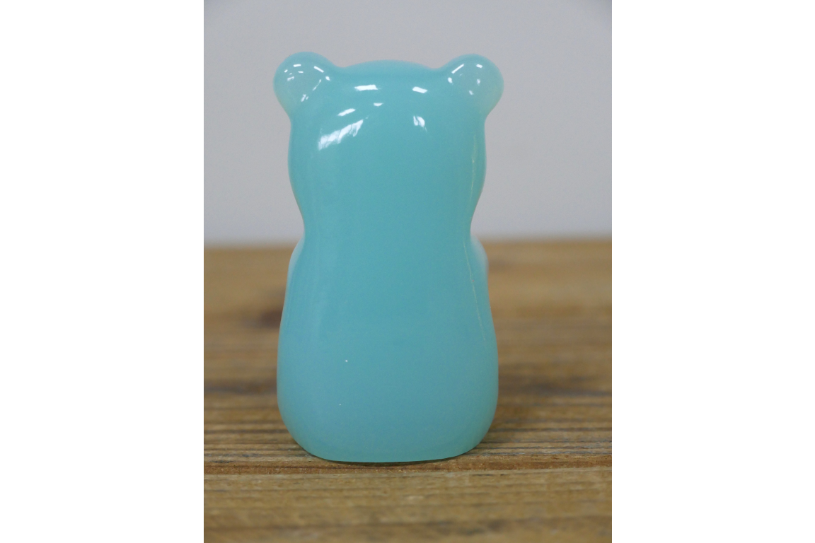Turquoise bear-shaped object on a wooden surface with a neutral background