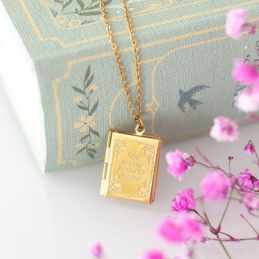 Gold book-shaped locket necklace with pink flowers on a decorative book