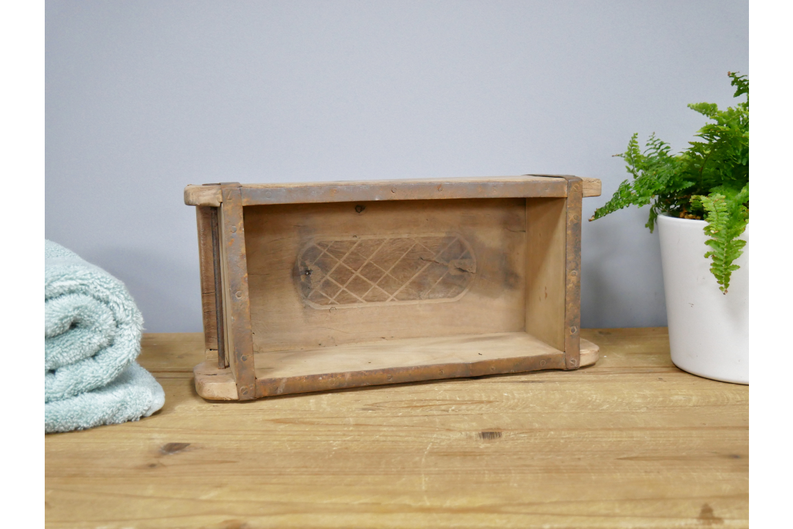 Wooden decorative brick mould box on a wooden surface with a plant and towel in the background