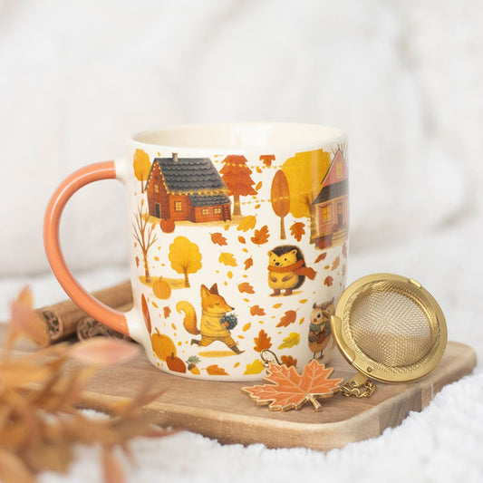 Mug with autumn-themed design featuring houses, trees, and animals on a wooden coaster with a tea ball.
