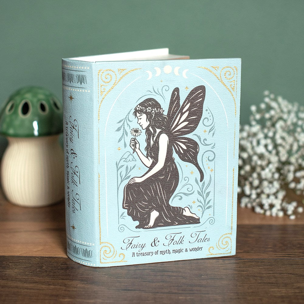 A decorative book storage box titled 'Fairy & Folk Tales' stands open on a wooden surface. The cover is pale blue with gold ornamental borders and a dark illustration of a fairy holding a flower.
