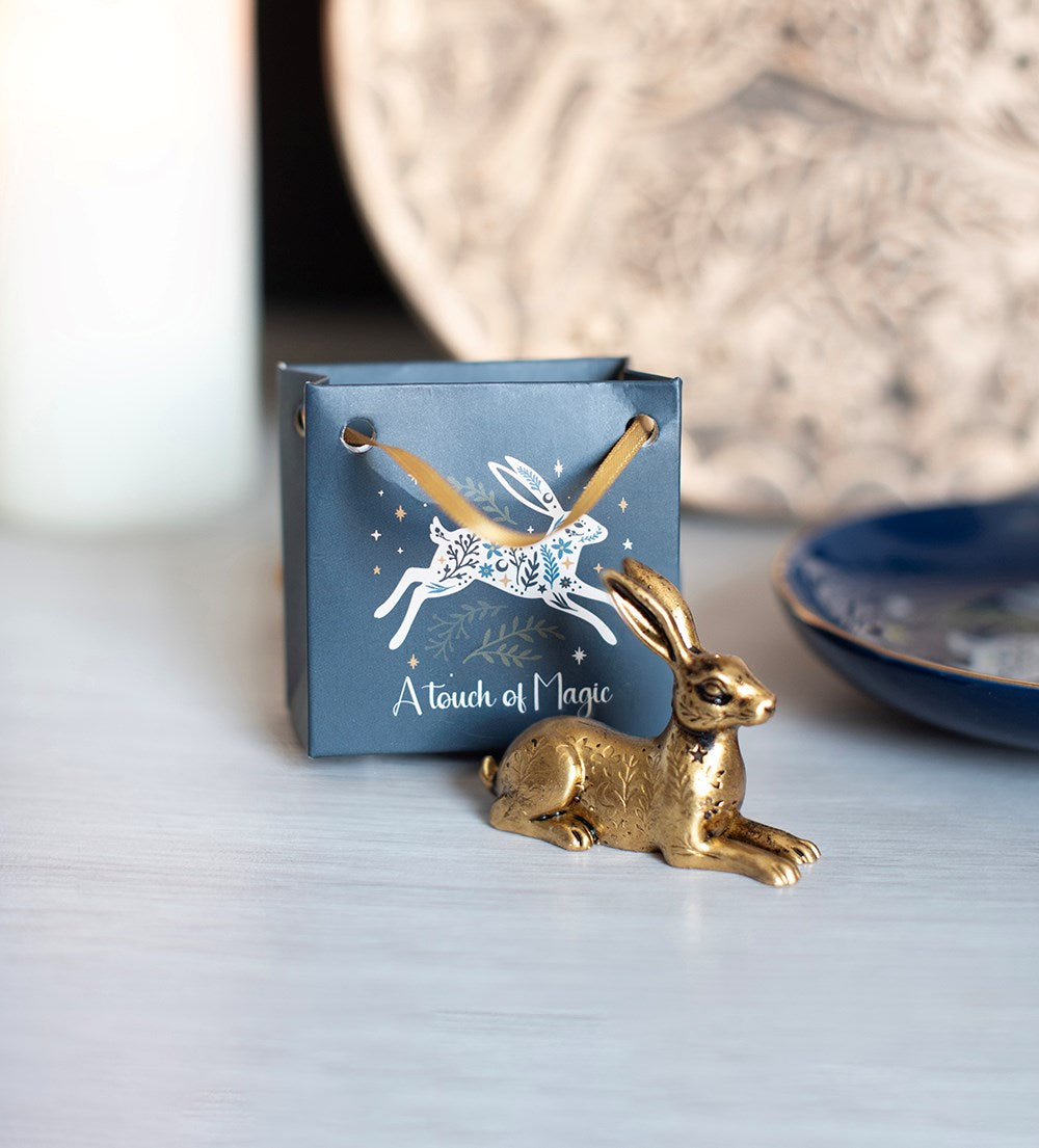 A small gold hare figurine placed in front of a blue gift box printed with a white hare and the words 'A touch of Magic'.