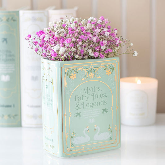 Decorative book-shaped vase with flowers on a table with candles in the background