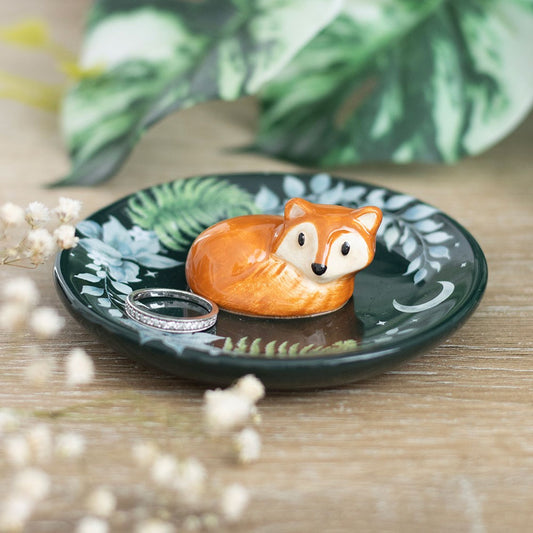 Decorative dish with a fox figurine and ring on a wooden surface with green leaves in the background