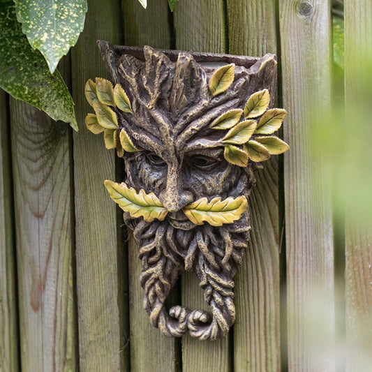 Decorative wall piece resembling a leafy green man on a wooden fence