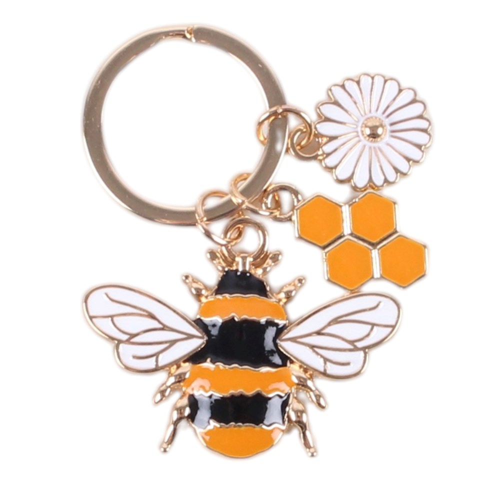 A gold-tone metal keychain featuring an enamel bee charm with black and orange stripes, white wings, and a white daisy flower charm with orange honeycomb accents, all attached to a split key ring.