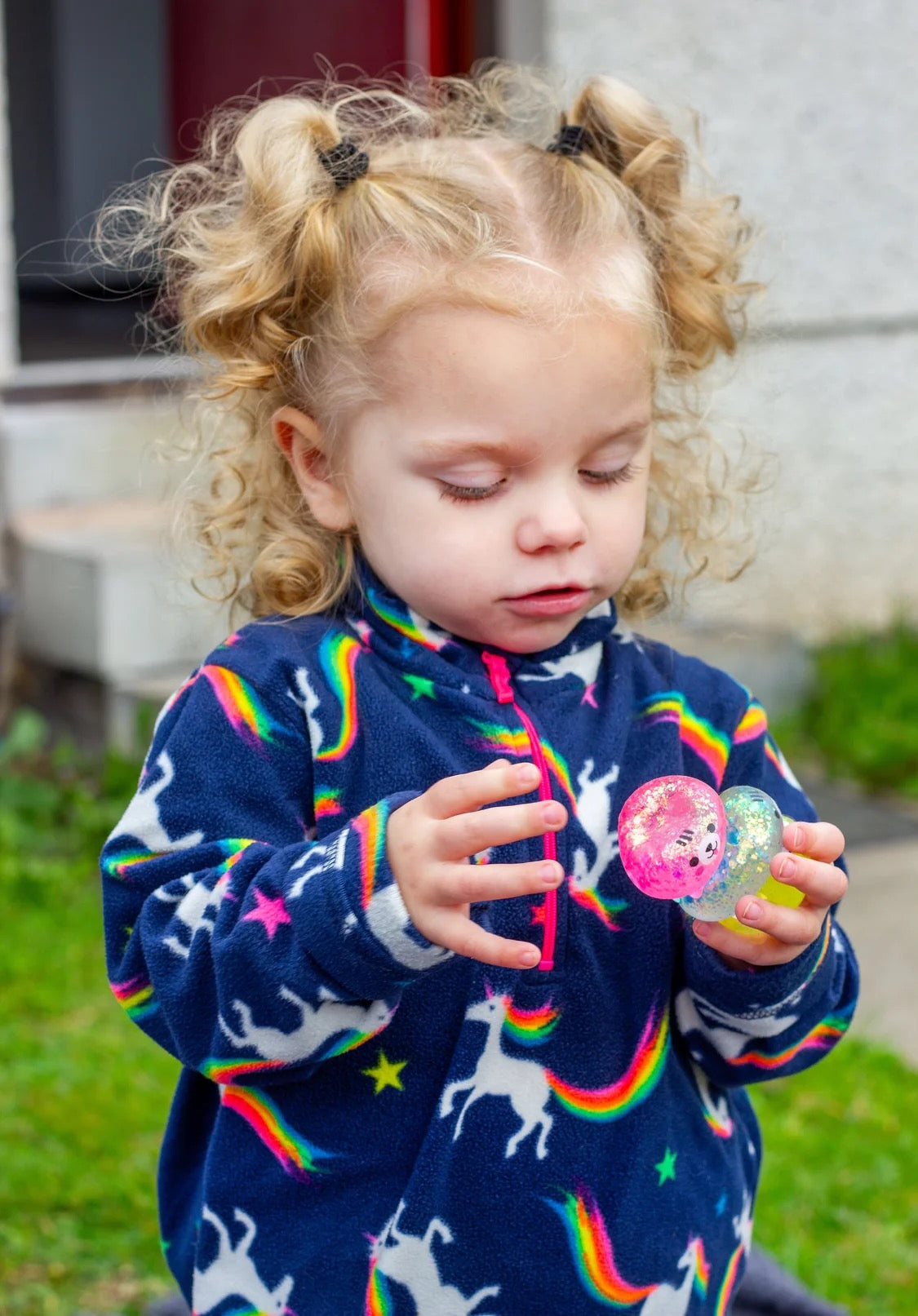 Child wearing a colourful sweater with rainbow patterns, playing outdoors with Scrunchems Sugar Squishy Kitties