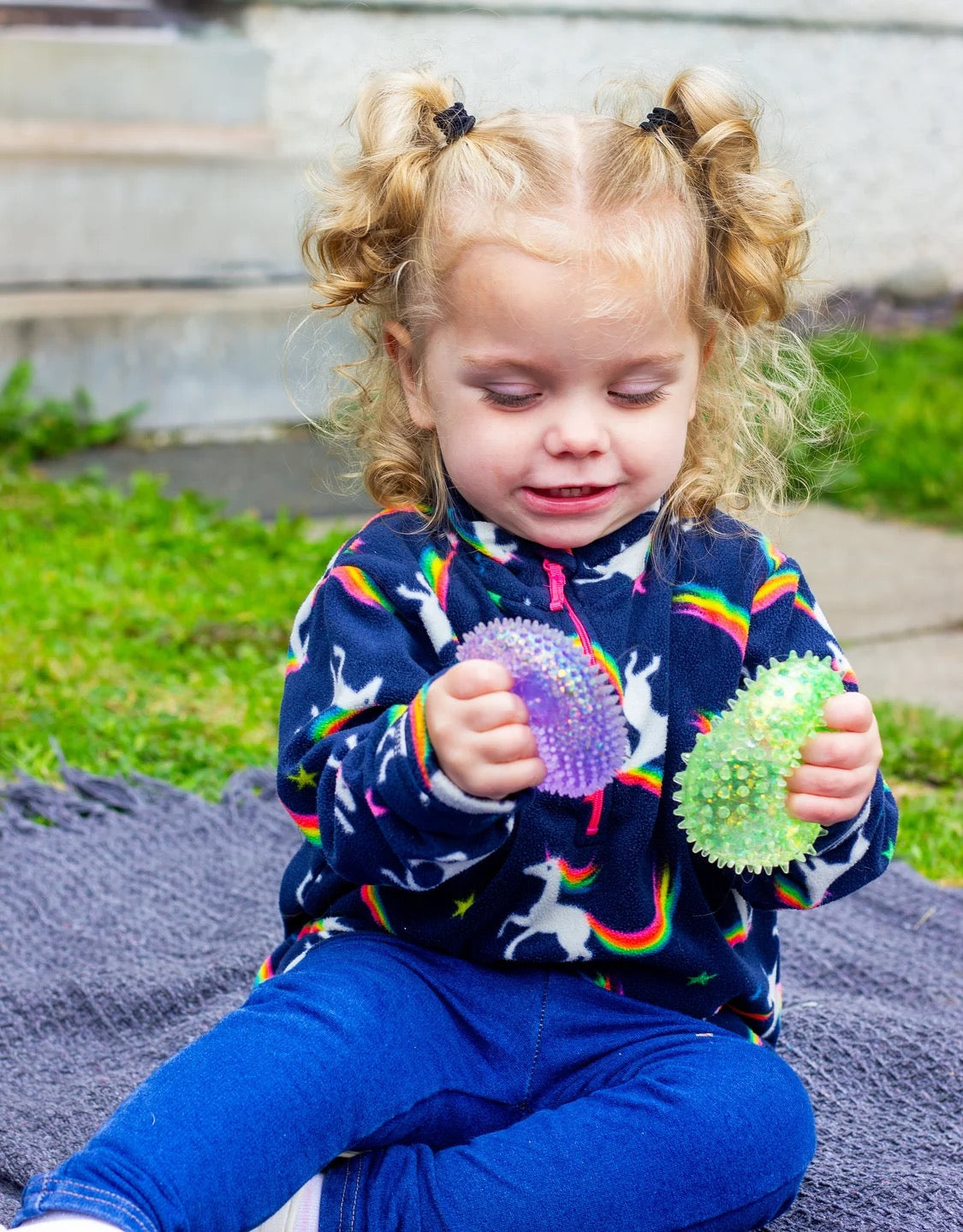 Child holding two textured Scrunchems Sensory Sugar Shapes outdoors on a blanket