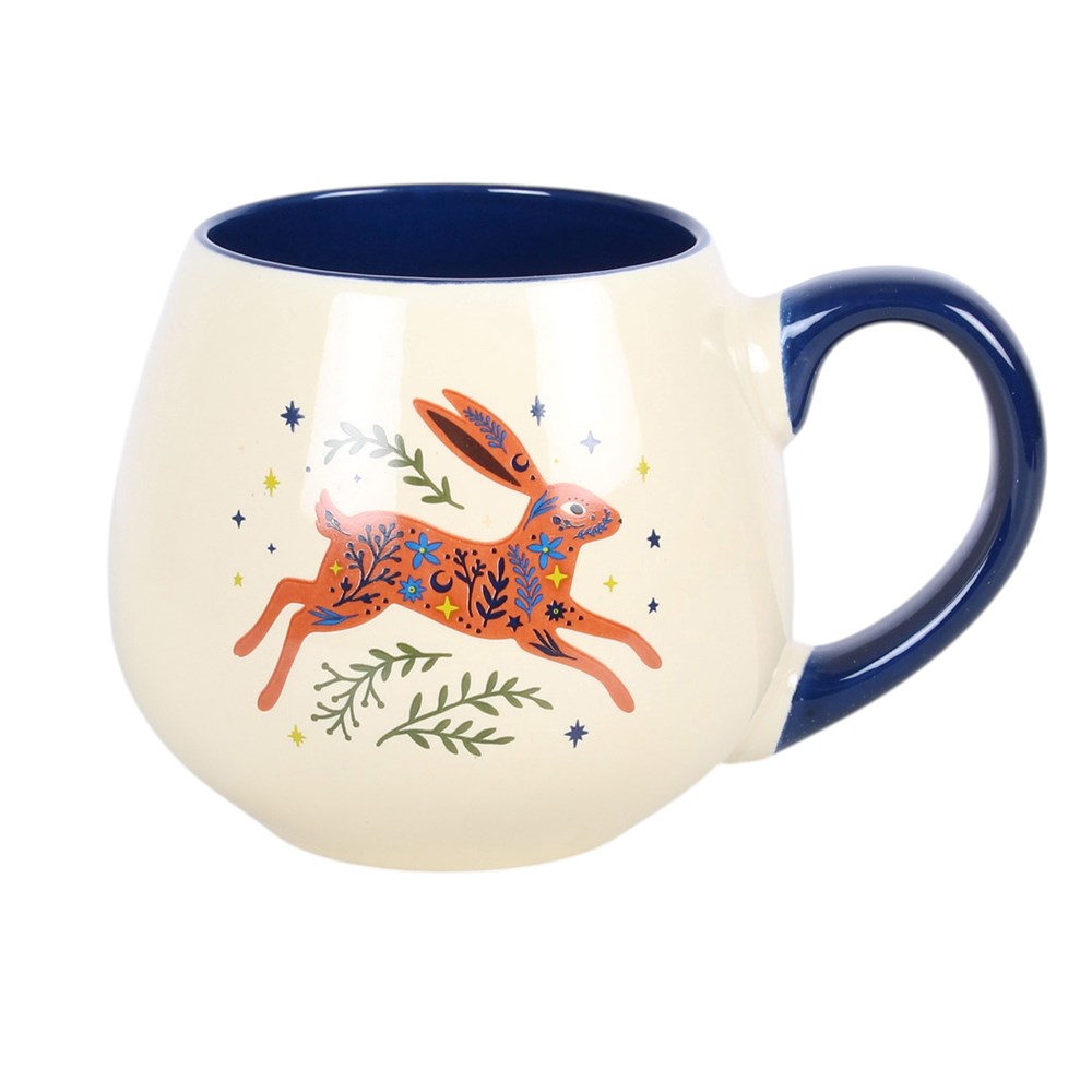 A cream mug with dark blue handle and a picture of a leaping hare with greenery and stars around it. I