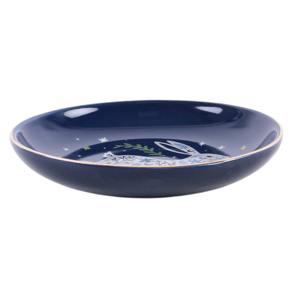 A round navy blue trinket dish with a hand-painted white rabbit and green leaves design on the inside, accented with a thin gold rim, shown against a plain white background.