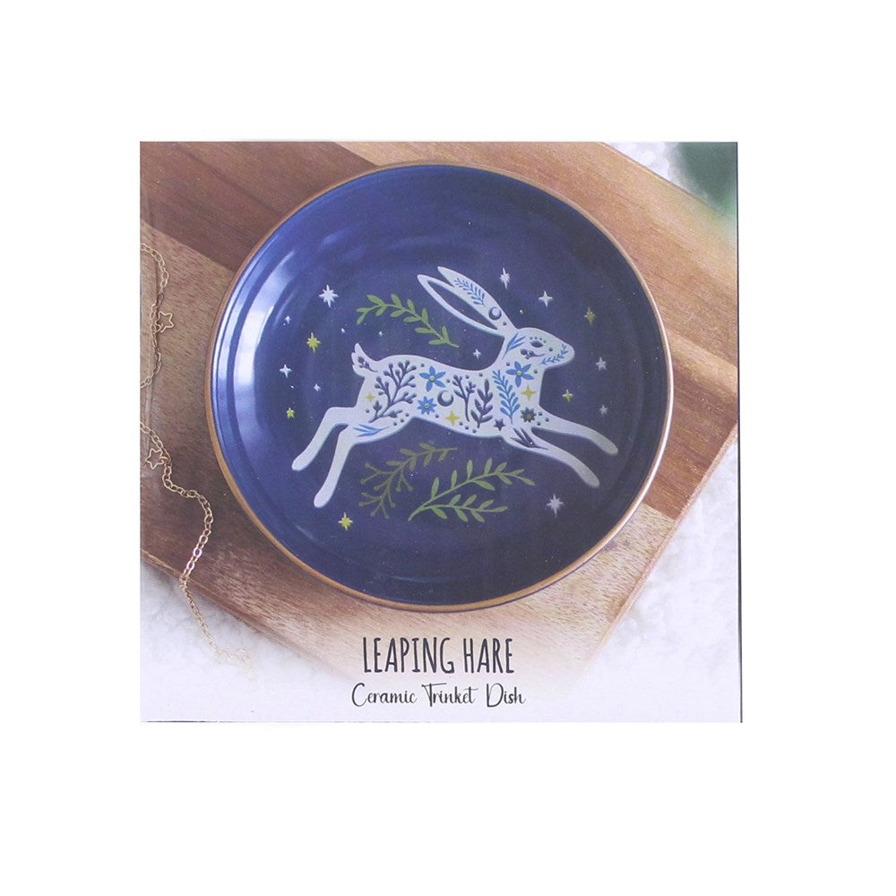 A square product card showing a ceramic trinket dish with a painted leaping hare design. The dish is dark blue with a white hare decorated with blue and green floral patterns, surrounded by small stars and green leaves.