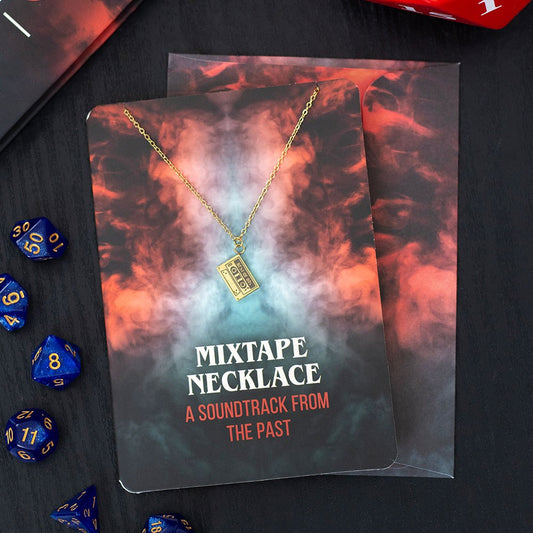 MIXTAPE NECKLACE packaging with gold coloured necklace on a dark surface with dice