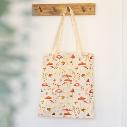 Tote bag with mushroom pattern hanging on a wooden hook against a white wall.
