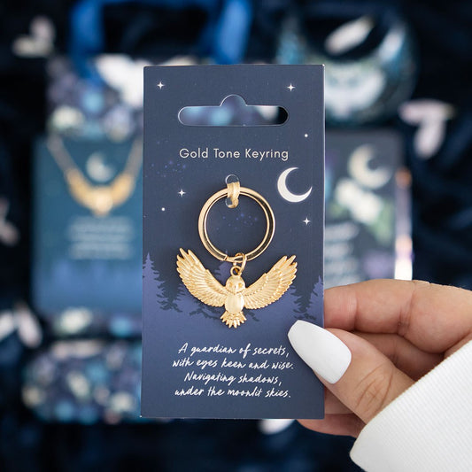 Gold tone keyring with owl design on a blue card held by a hand.