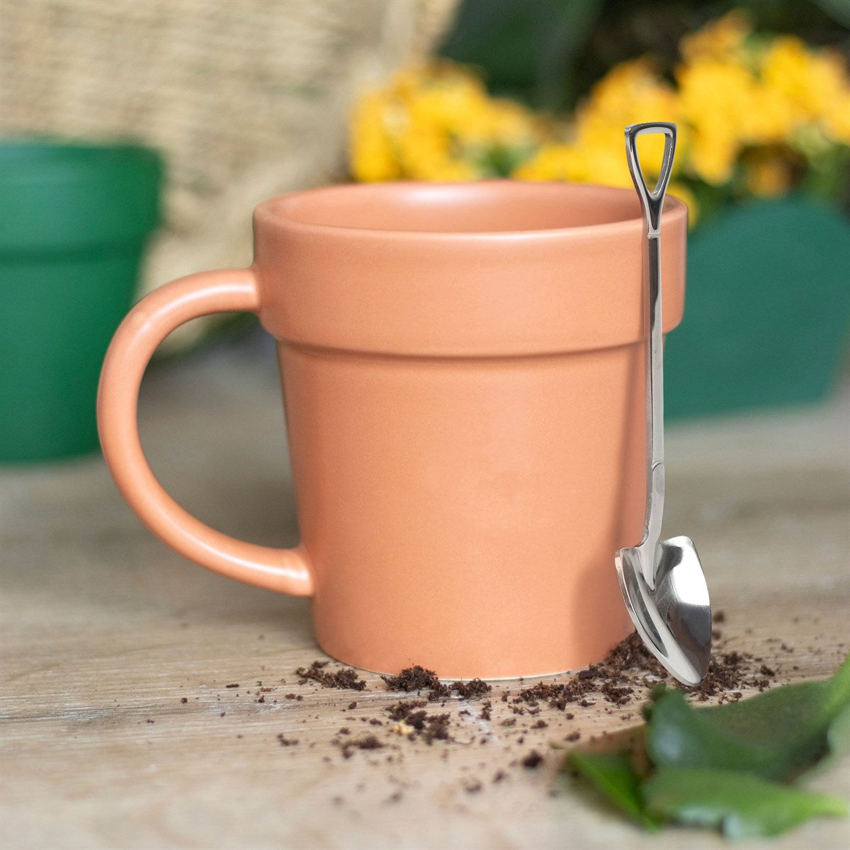 Terracotta mug with a spoon on a wooden surface with soil and leaves
