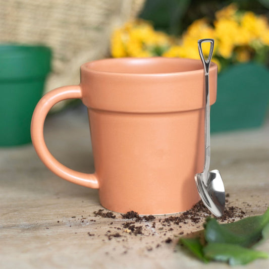 Terracotta mug with a spoon on a wooden surface with soil and leaves