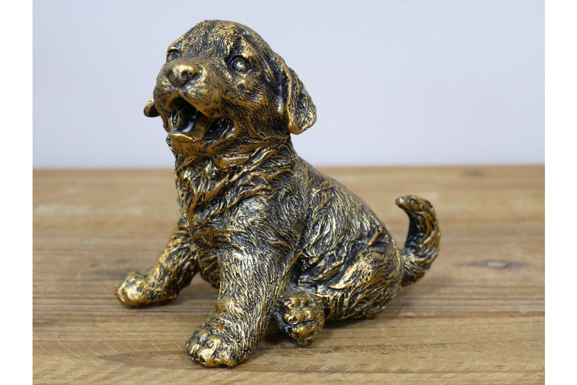 Bronze statue of a puppy on a wooden surface with a light gray background