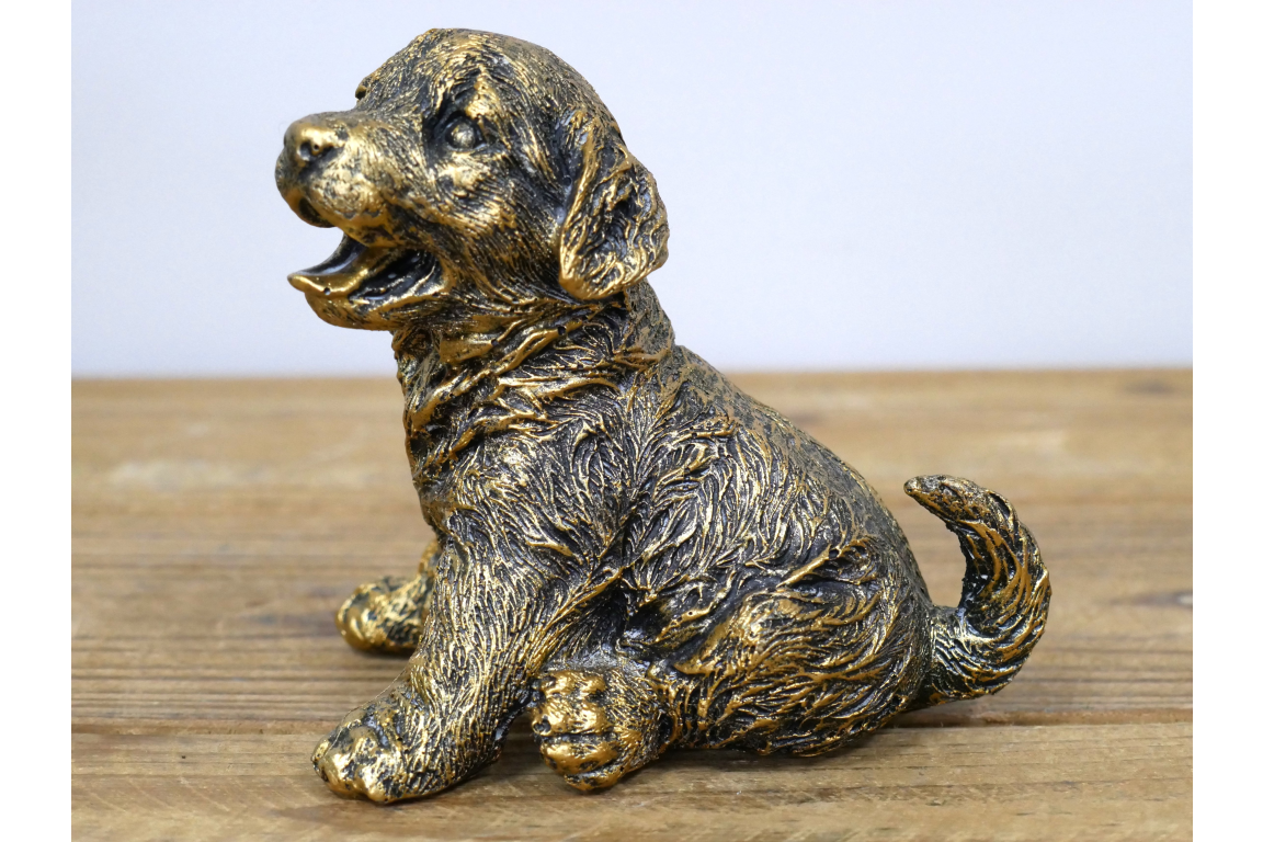Bronze statue of a sitting dog on a wooden surface with a light blue background
