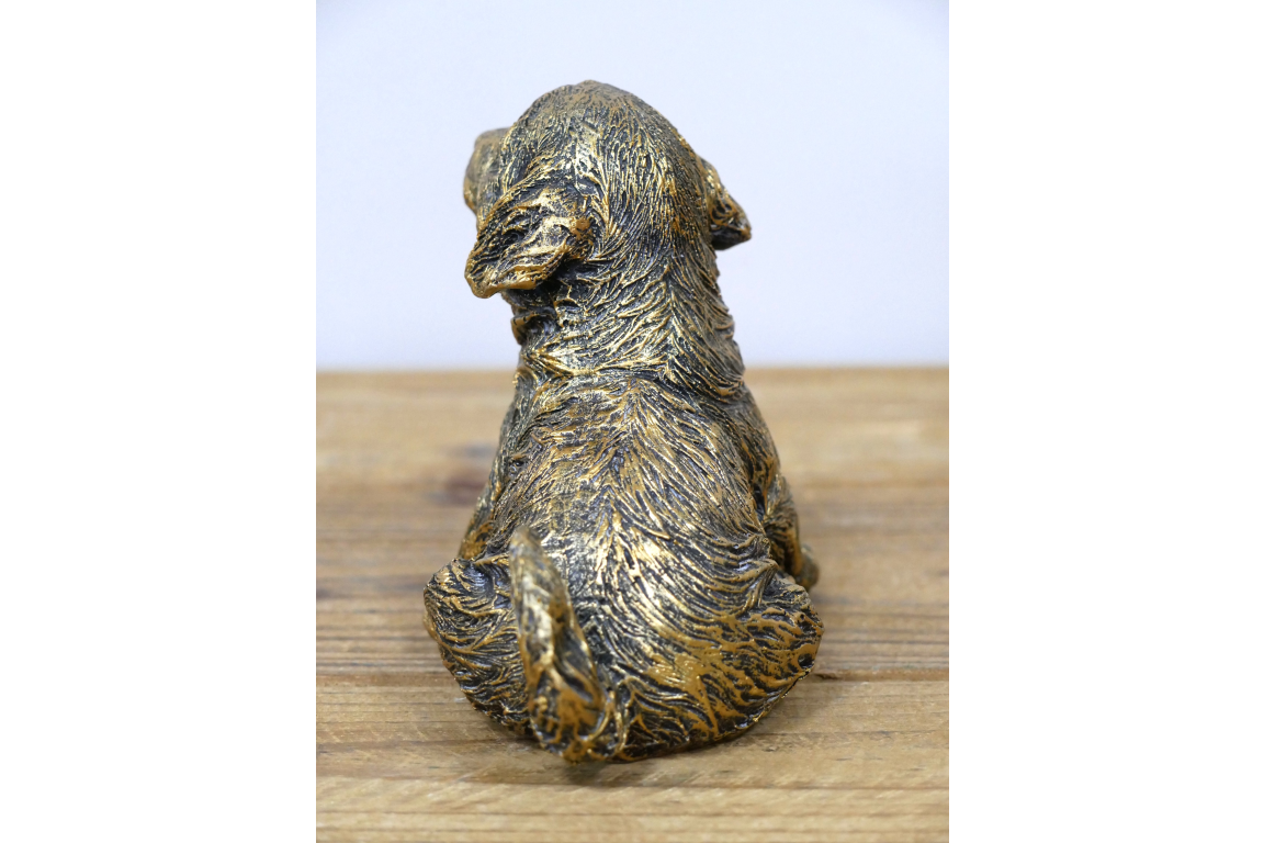 Bronze statue of a dog on a wooden surface with a white background