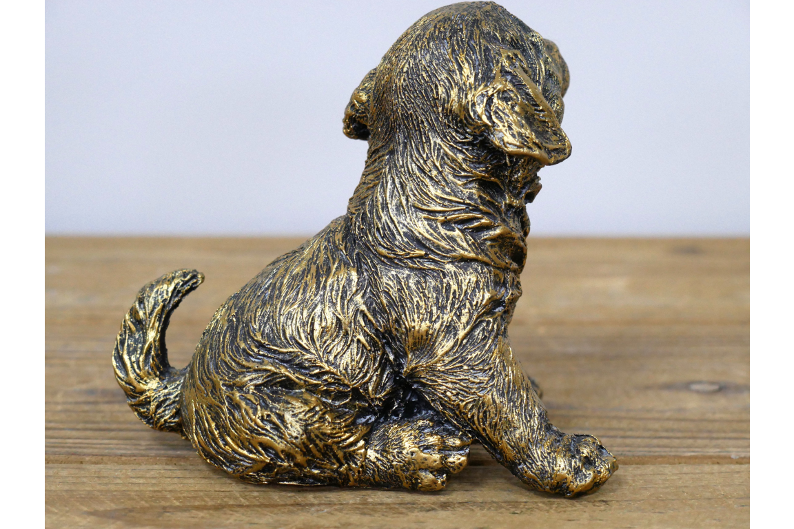 Bronze statue of a puppy on a wooden surface with a light gray background