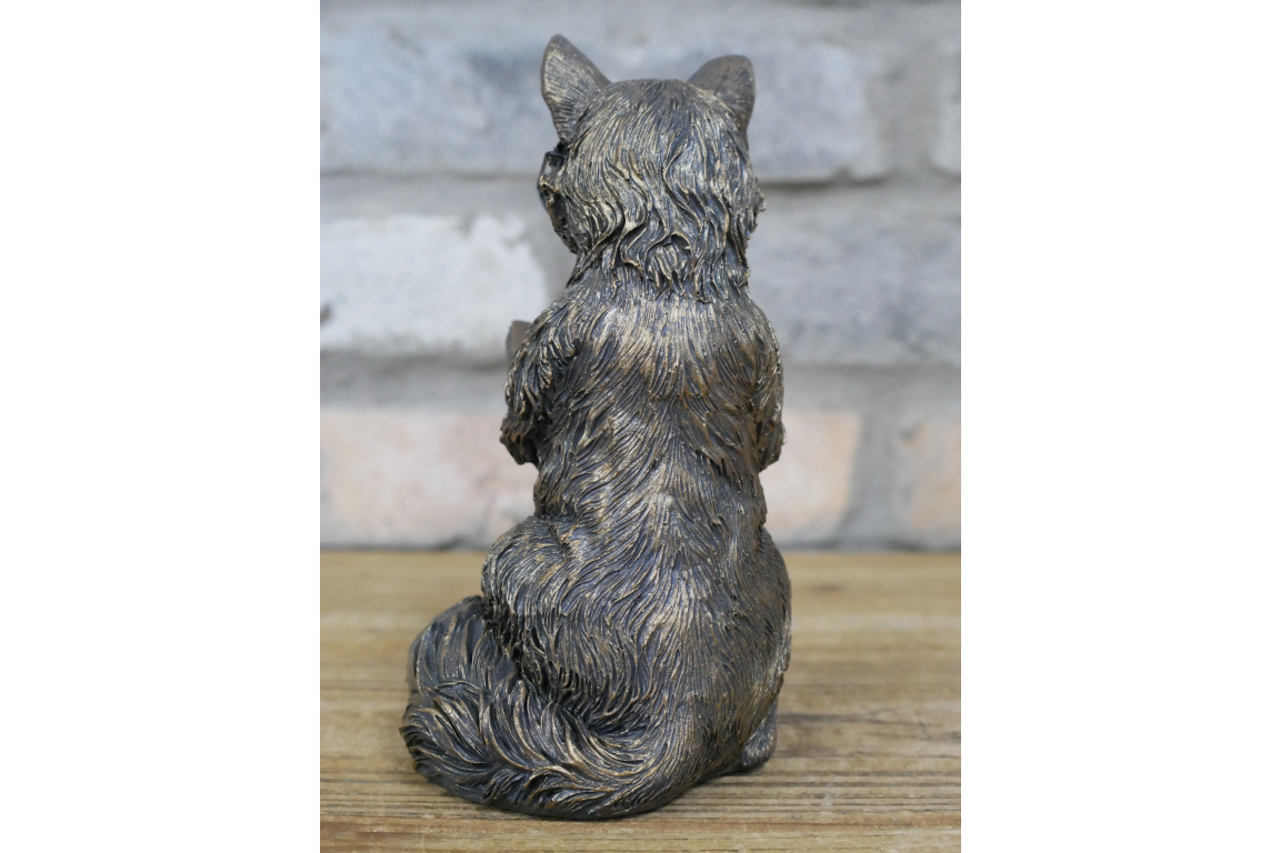 Bronze statue of a sitting fox on a wooden surface with a stone wall background