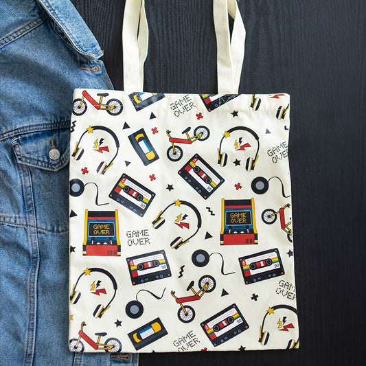 Tote bag with retro-themed design featuring cassette tapes, bikes, and 'Game Over' signs on a white background.