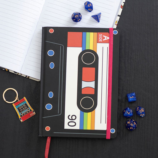 Notebook with cassette tape design, dice, and keychain on a black surface