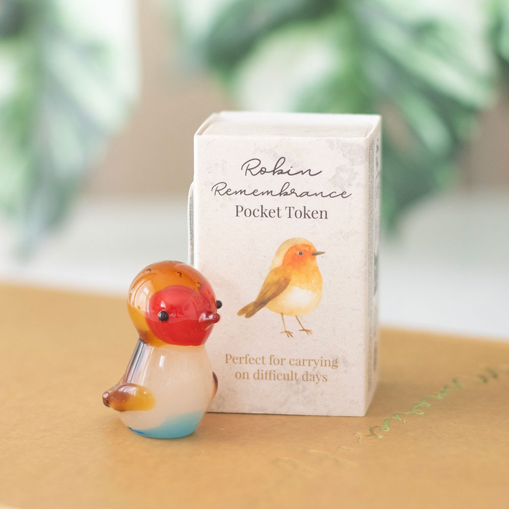 Glass robin figurine with a box labeled 'Robin Remembrance Pocket Token' on a wooden surface.