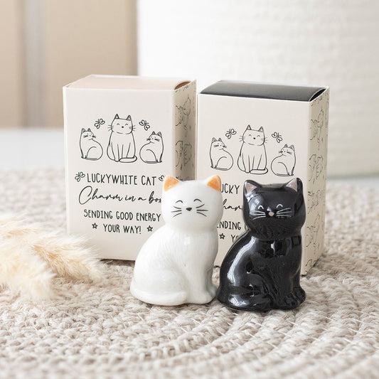 White and black cat-shaped charms with packaging on a textured surface