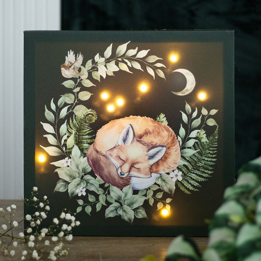 Decorative wall art with a fox surrounded by leaves and flowers, illuminated by small lights.