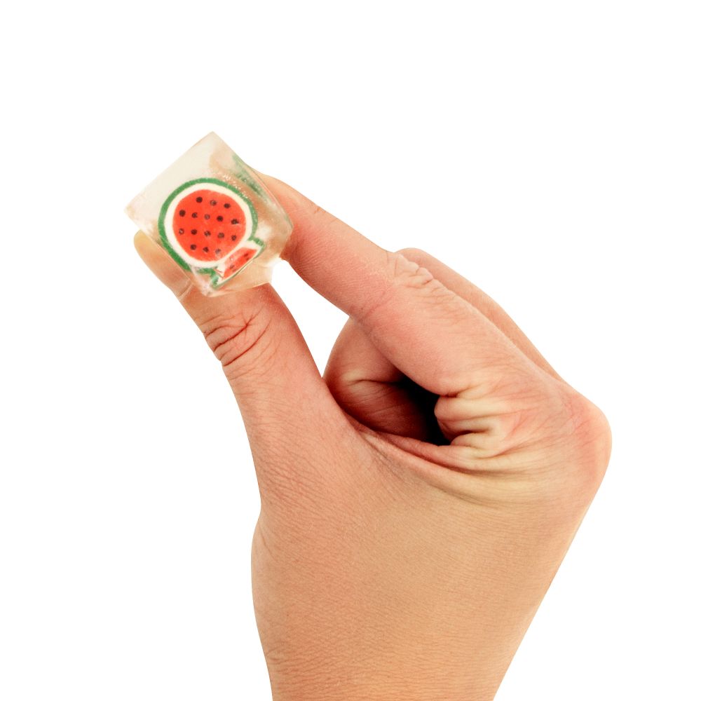 Hand holding a small watermelon Squishy Ice Cubes candy on a white background