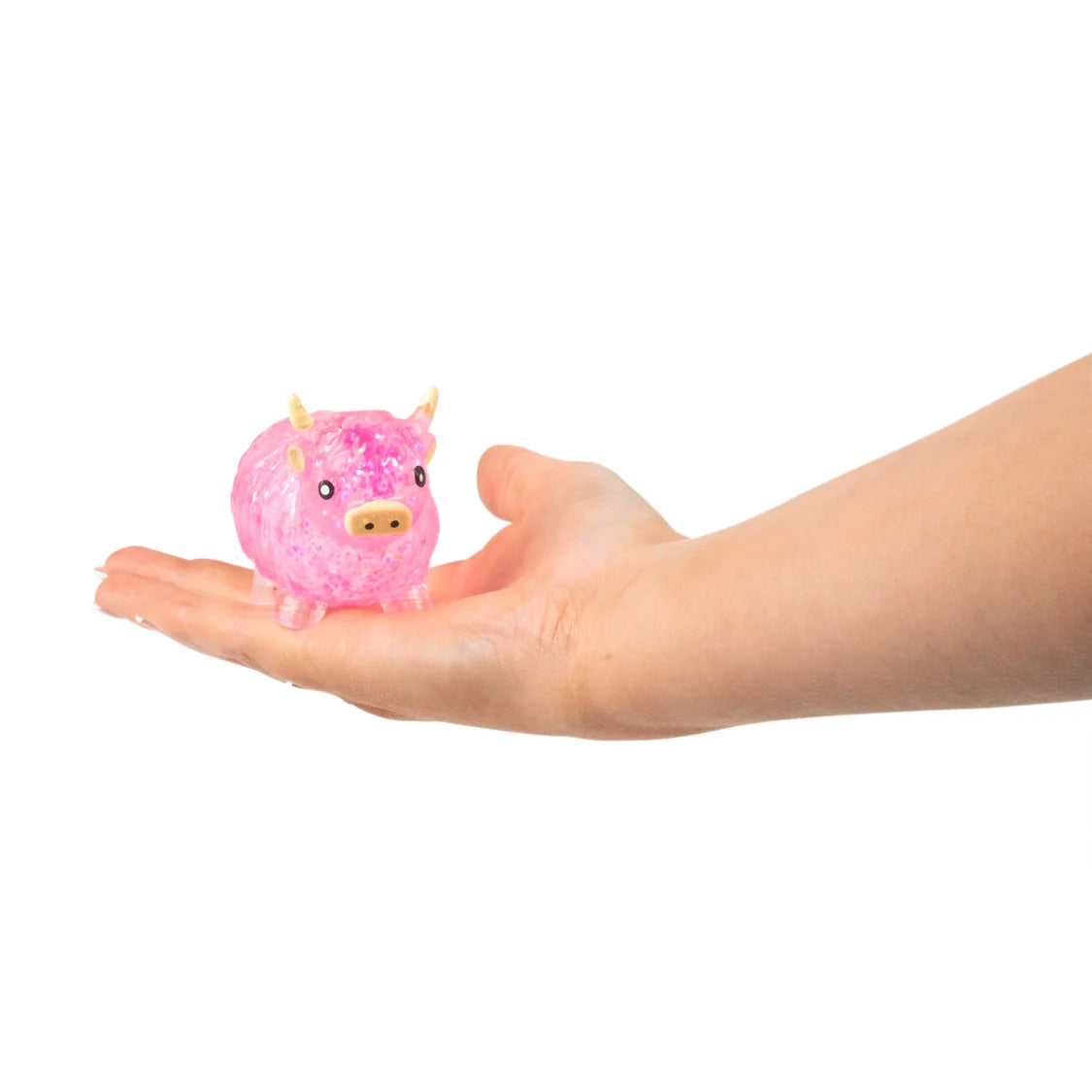 A small pink glittery sugar highland cow toy with small horns sits on an open human hand against a plain white background.
