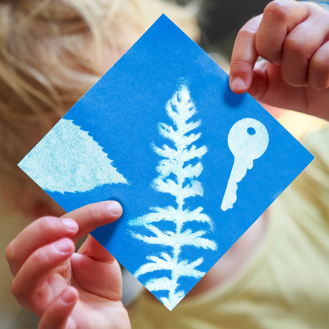 Blue square card with white leaf and key design held by hands against a blurred background