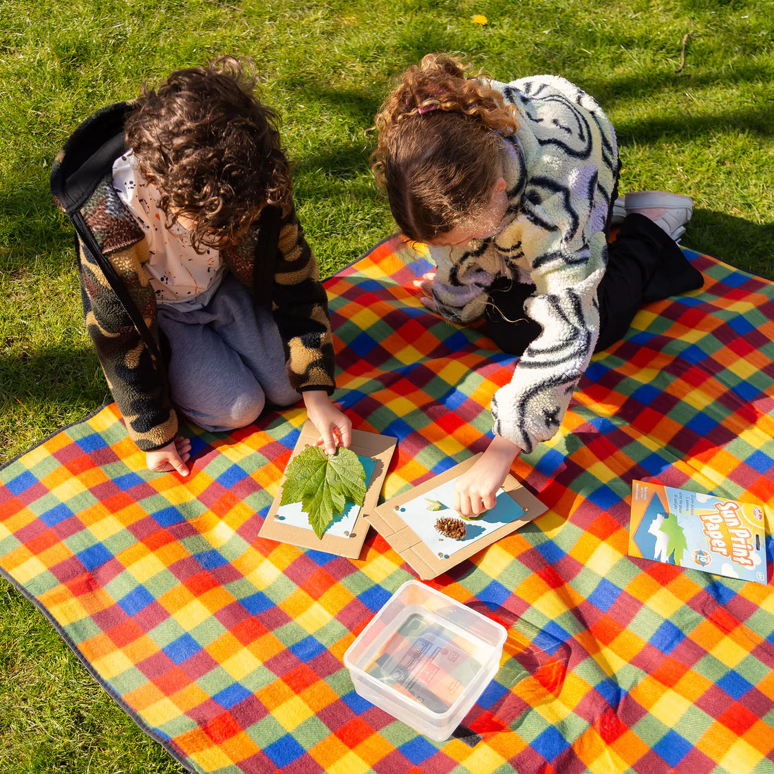 Two children on a colorful blanket outdoors, engaging with nature-themed cards.