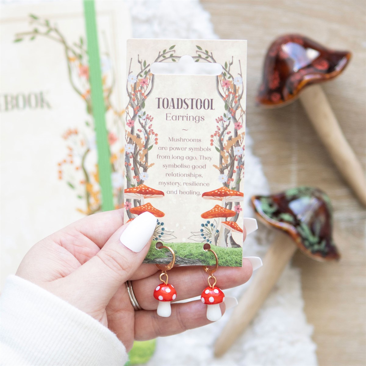 Toadstool earrings held in front of their packaging with a blurred background