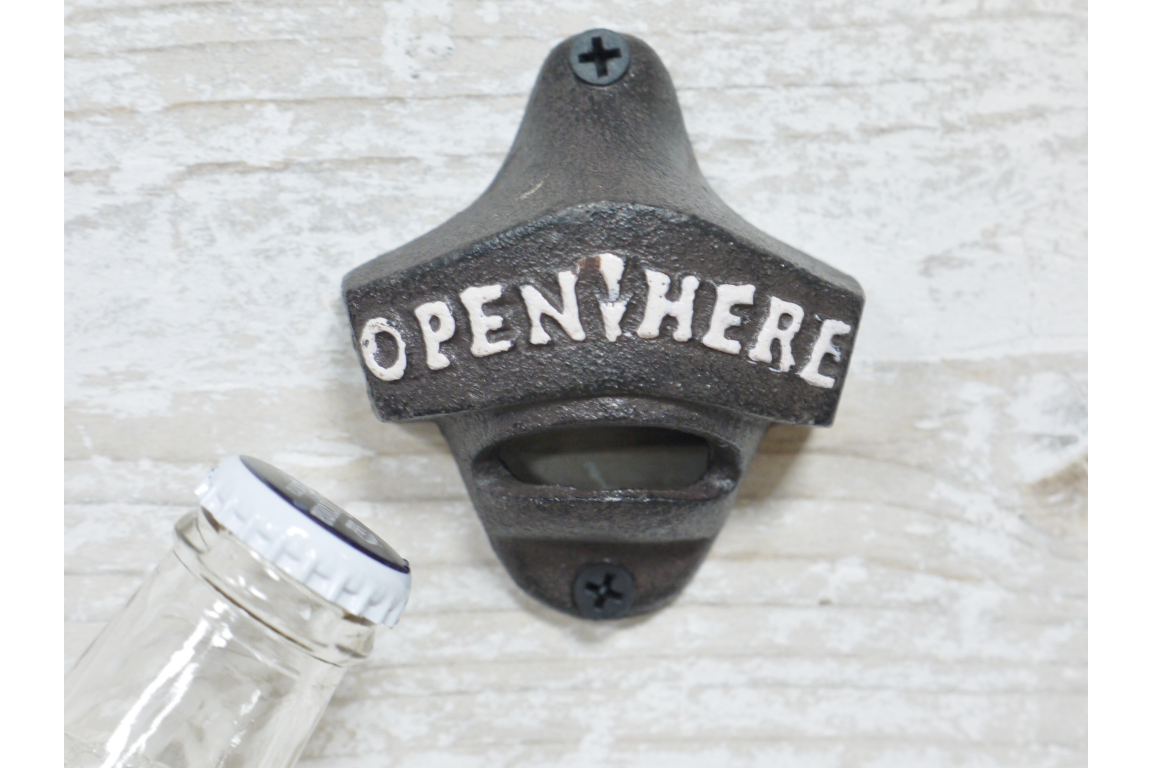 Wall-mounted bottle opener with 'Open Here' text on a textured surface