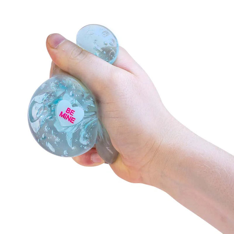 Hand holding a Scrunchems Kind Heart Squish Bear with 'Be Mine' text on a white background