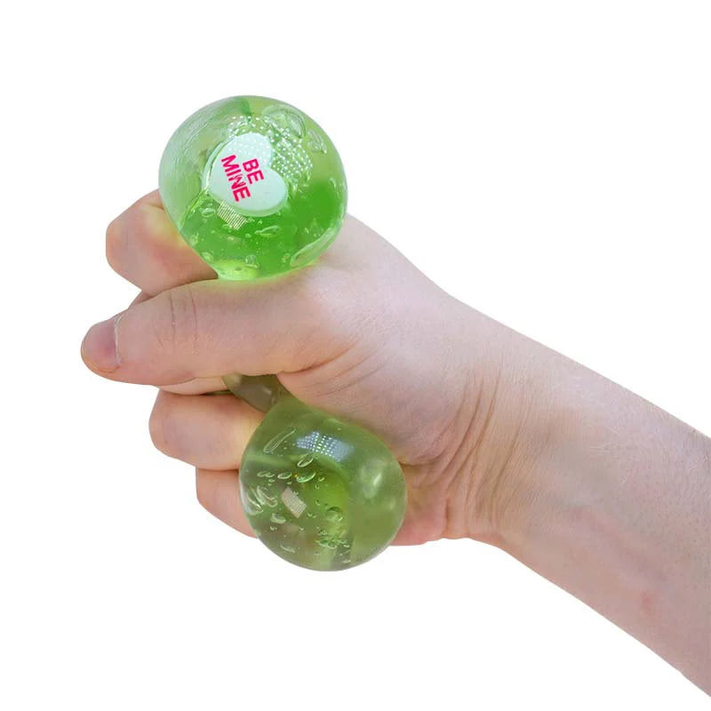 Hand holding a green Scrunchems Kind Heart Squish Bear with 'Be Mine' text on a white background