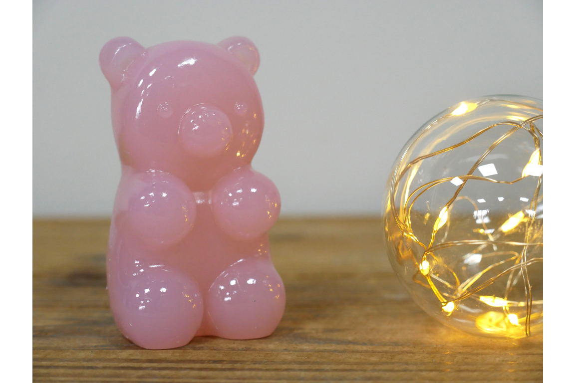 Pink gummy bear-shaped ornament on a wooden surface with a string light in the background.