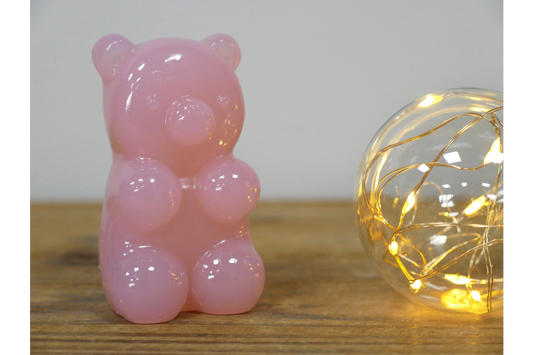 Pink gummy bear-shaped ornament on a wooden surface with a string light in the background.